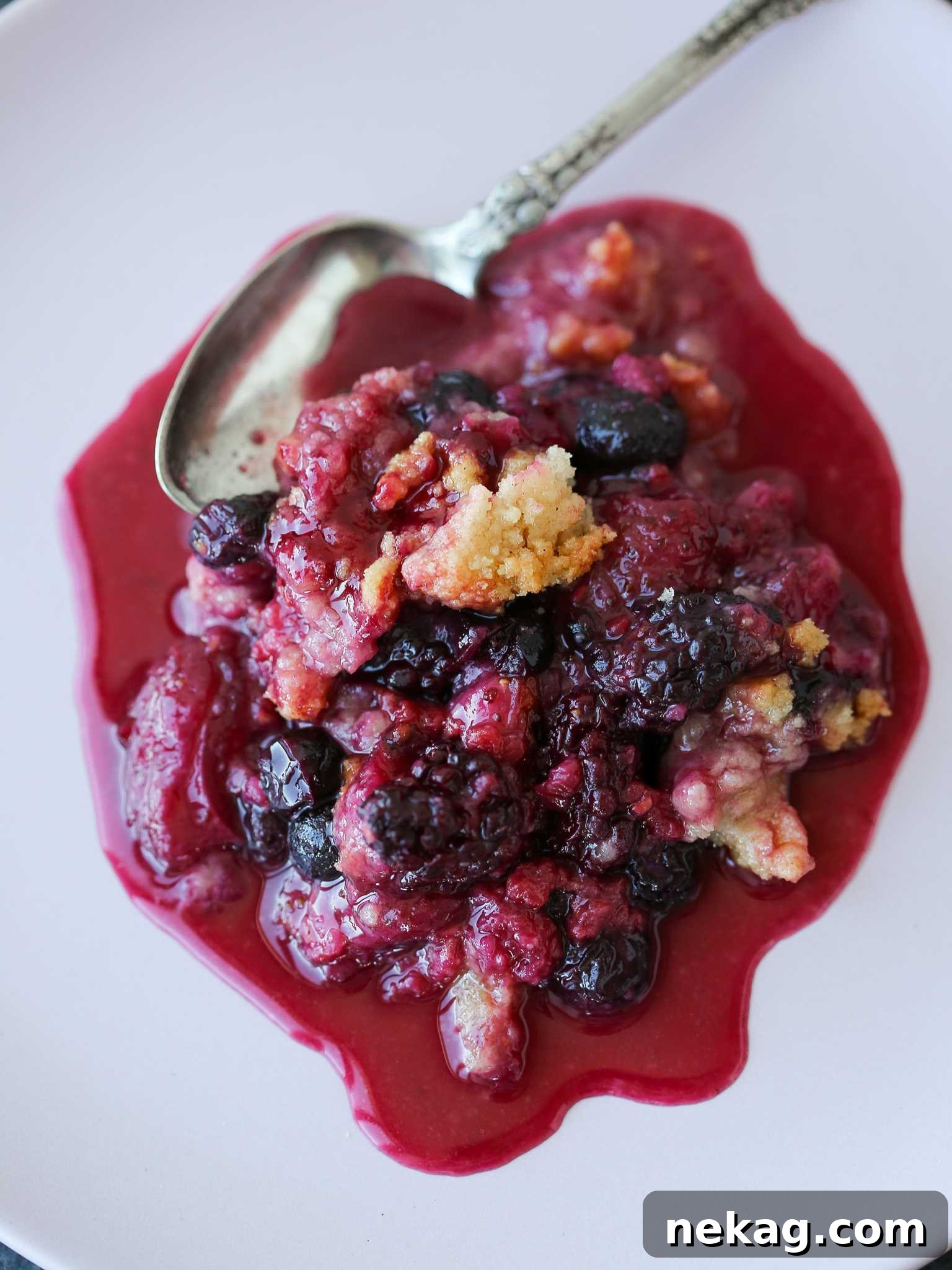 Warm Berry Crumble Bliss 3 A serving of mixed berry crumble on a white plate, topped with a scoop of vanilla ice cream and a fresh berry garnish.
