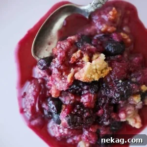 Warm Berry Crumble Bliss 5 A close-up of a mixed berry crumble with a silver spoon taking a portion, highlighting the golden topping and juicy filling.