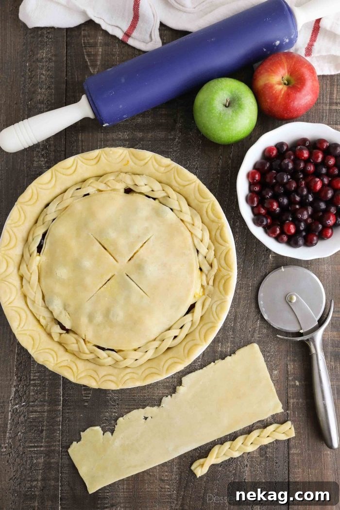 A close-up of an unbaked Cranberry Apple Pie with a beautifully braided top crust and a scalloped edge.