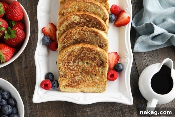 Ultimate Cinnamon French Toast Tutorial 10 A beautifully plated dish of cinnamon French toast, adorned with fresh berries, a dollop of whipped cream, and a small pitcher of maple syrup on the side.