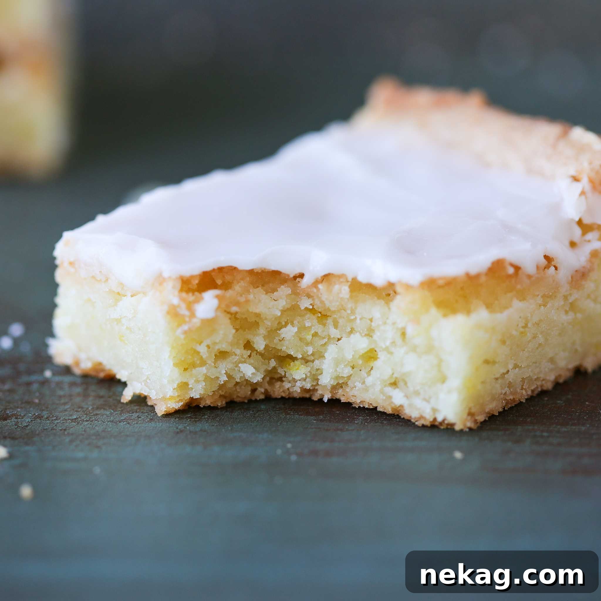 A hand serving a slice of lemon blondie on a plate, showing its moist texture and shiny glaze.