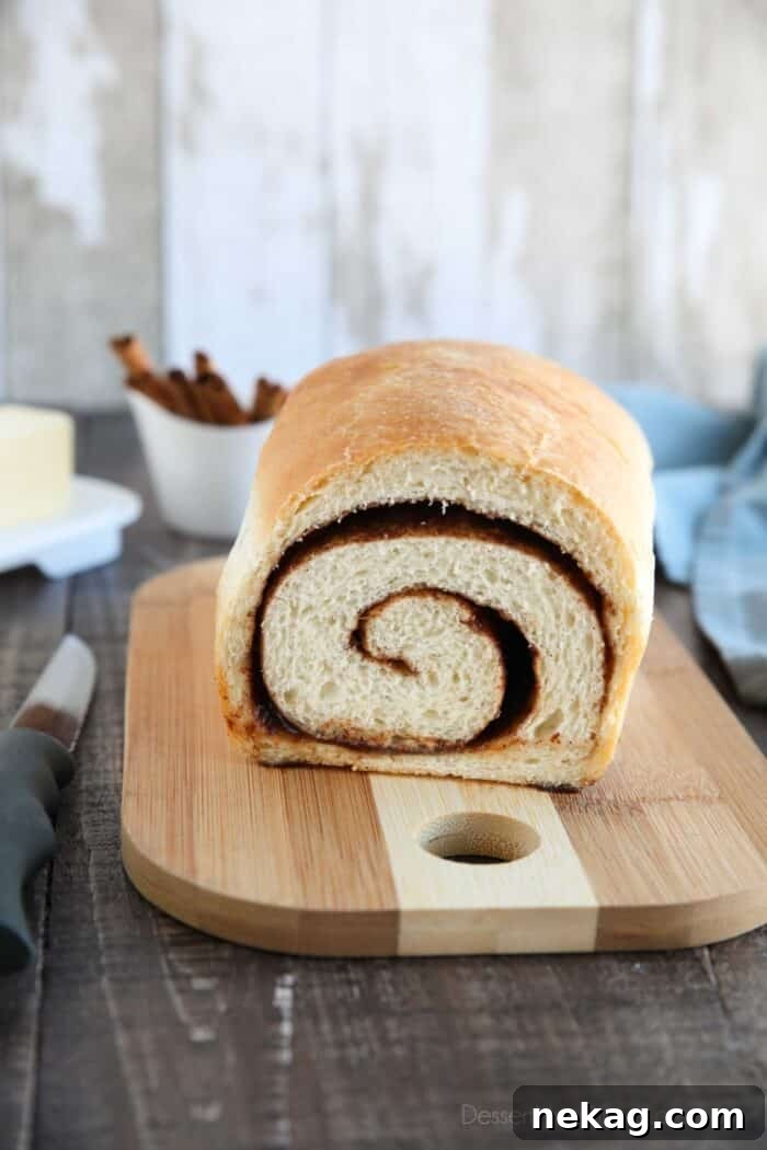Effortless Cinnamon Swirl Delight 2 A beautifully baked loaf of cinnamon swirl bread on a wooden cutting board, with one slice already removed revealing the intricate cinnamon pattern within.