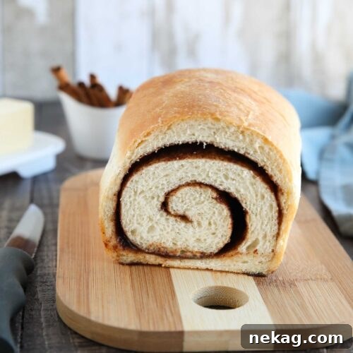 Loaf of cinnamon bread on a cutting board with a slice removed to show the cinnamon swirl on the inside.