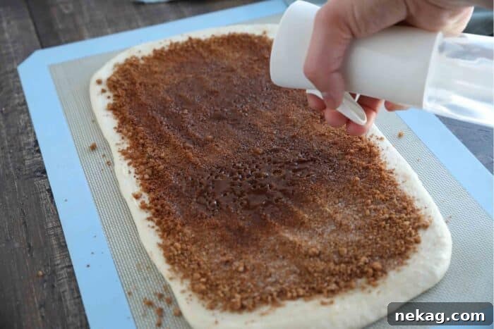 Effortless Cinnamon Swirl Delight 6 A close-up of the cinnamon sugar mixture spread over the buttered dough, being lightly sprayed with water to moisten it.