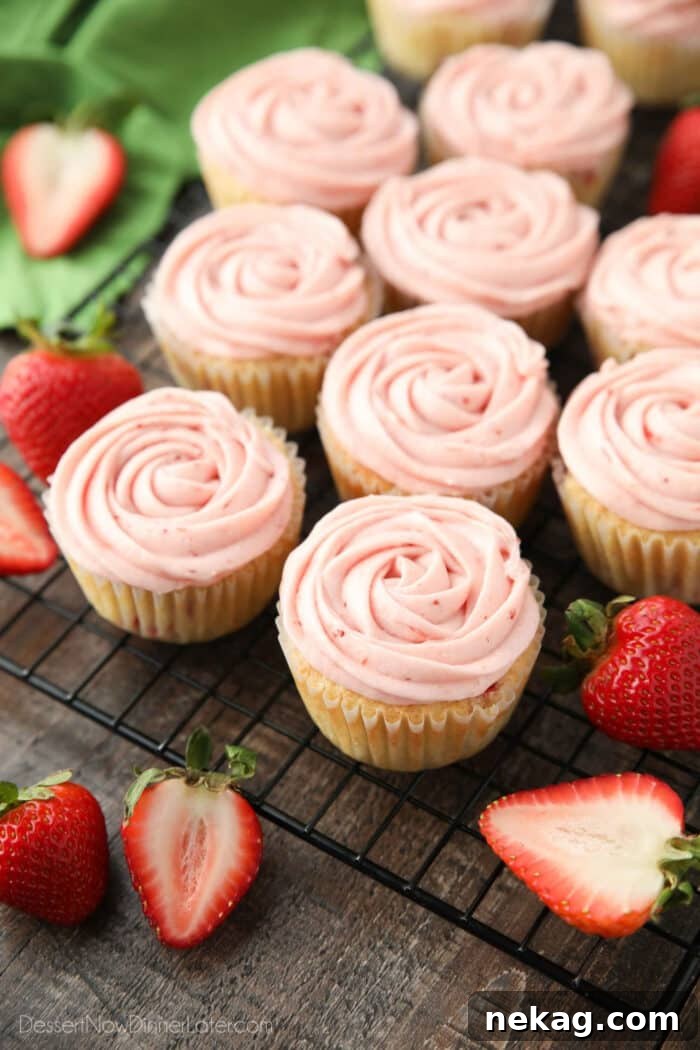 Freshly baked strawberry cupcakes, each topped with a vibrant pink rosette of strawberry buttercream frosting.
