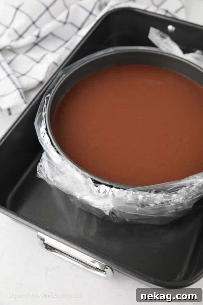 Decadent Triple Chocolate Cheesecake 8 A chocolate cheesecake in a springform pan, visibly wrapped in a layer of foil and then an additional plastic slow cooker liner, ready to be placed into a water bath for baking.
