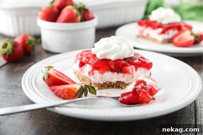 Strawberry Delight Video Recipe 11 A single, inviting square of Strawberry Delight presented on a plate, featuring all its delicious layers—the crumbly graham cracker crust, the creamy cheesecake, and the glistening strawberry jello with fresh fruit—beautifully topped with a dollop of whipped cream.