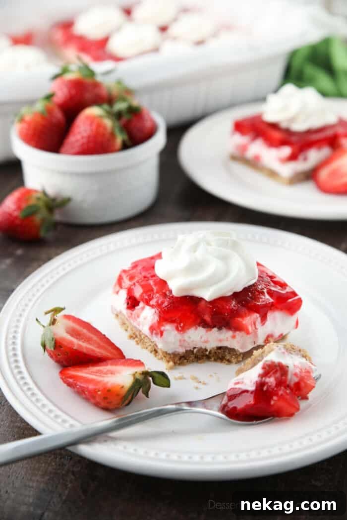 Strawberry Delight Video Recipe 3 A delectable serving of Strawberry Delight on a plate, with a fork gently scooping into its layers, revealing the irresistible textures of the crunchy crust, smooth cheesecake, and fresh fruit jello.