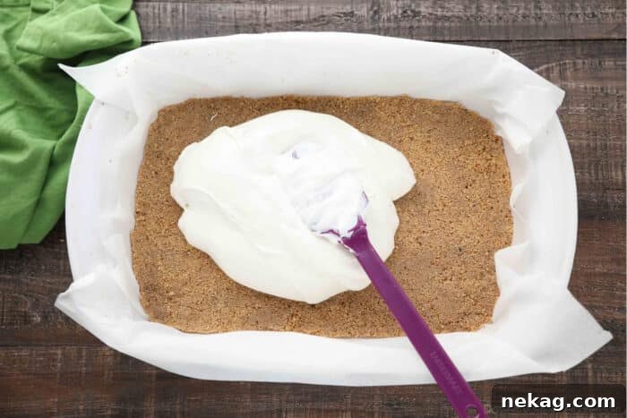 Strawberry Delight Video Recipe 6 A spatula smoothly spreading the luscious no-bake cheesecake filling over a perfectly baked and cooled graham cracker crust in a 13x9-inch pan, creating a pristine, even layer for the next stage of the dessert.