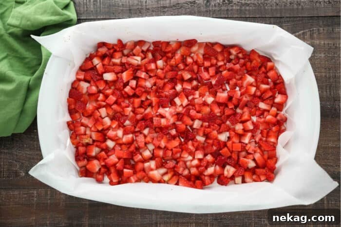 Strawberry Delight Video Recipe 7 A generous scattering of bright red, freshly diced strawberries forming an appealing layer atop the smooth, white no-bake cheesecake, contrasting beautifully and preparing the dessert for its final Jello topping.