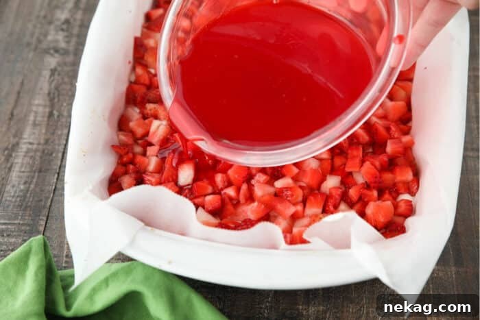 Strawberry Delight Video Recipe 9 A steady stream of warm, glistening strawberry jello mixture being carefully poured over the vibrant fresh strawberries, ensuring an even coating that will bind the fruit and create a beautiful, set layer.
