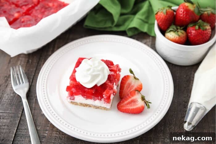 Strawberry Delight Video Recipe 10 An elegantly portioned piece of Strawberry Delight resting on a plate, garnished with a single halved fresh strawberry on the side, highlighting the dessert's freshness and visual appeal.