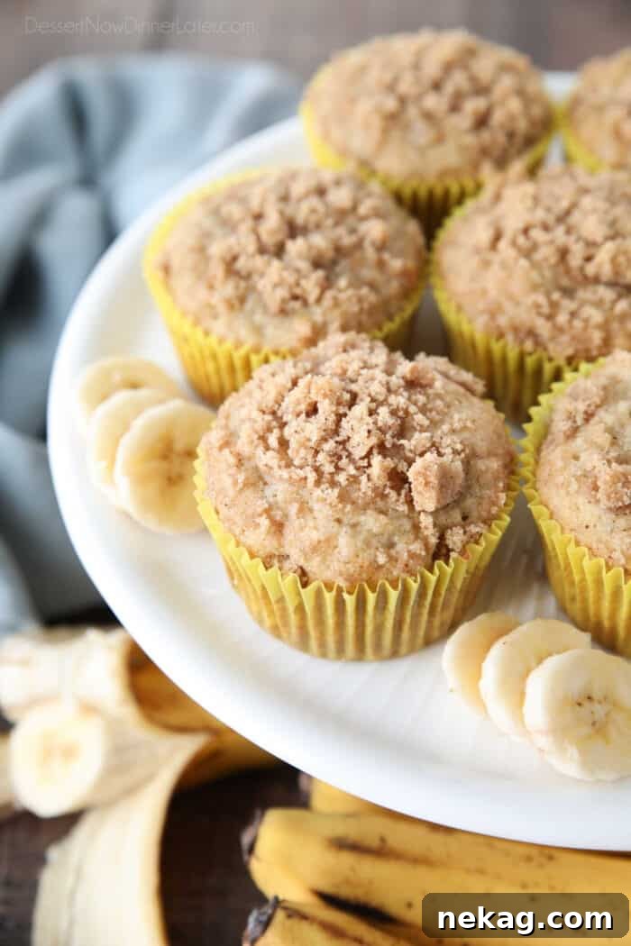 Golden Banana Streusel Muffins 2 White cake plate with banana muffins in yellow wrappers with crumb streusel on top and slices of banana on the sides.