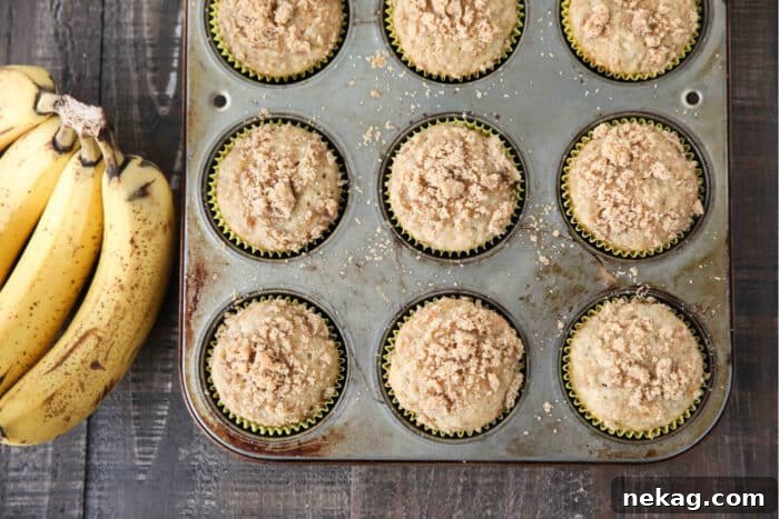 Golden Banana Streusel Muffins 8 Baked banana crumb muffins in cupcake tin with bunch of bananas on the side.