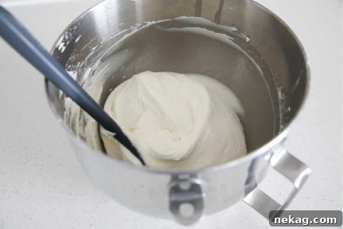 Whipped Cream Cheese Frosting Recipe and Video Tutorial 13 Whipped cream cheese frosting in a mixing bowl with a spatula, showcasing its smooth texture.