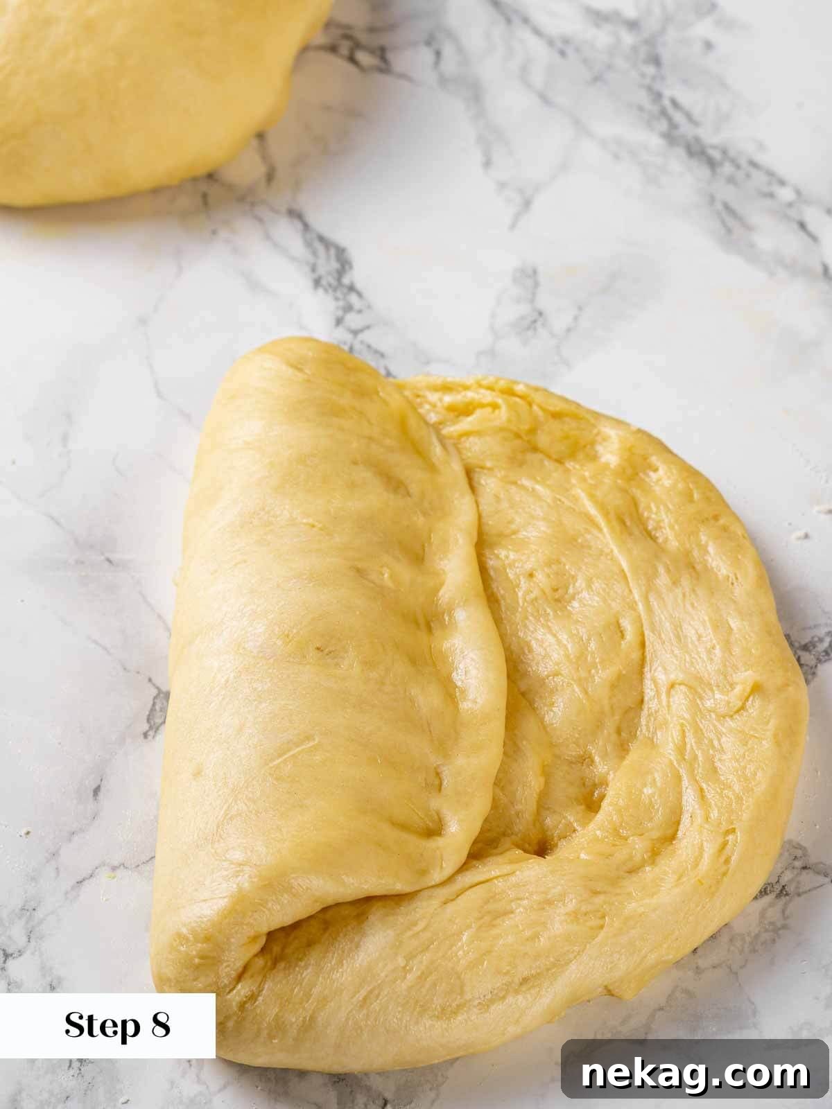 A baker demonstrating the technique of folding and sealing brioche dough to create a log shape.