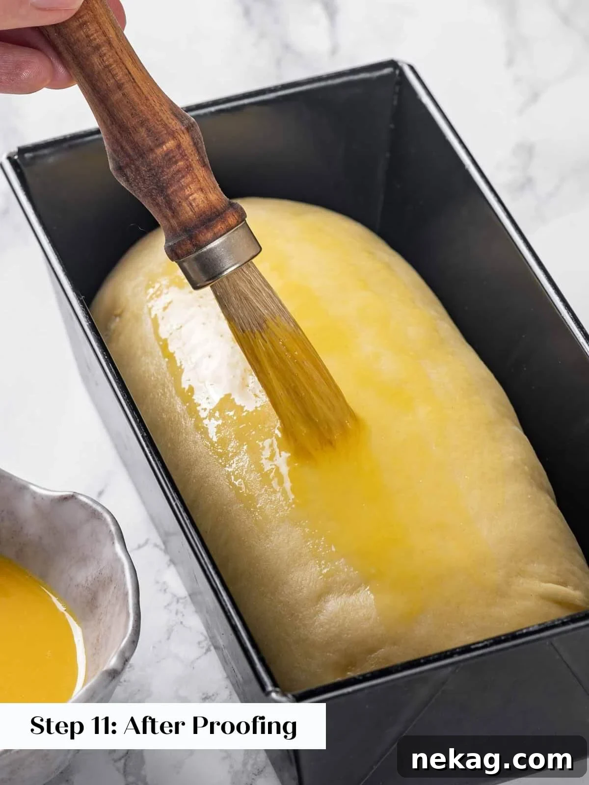 A baker carefully applying an egg wash to the surface of brioche dough in a loaf pan before baking.