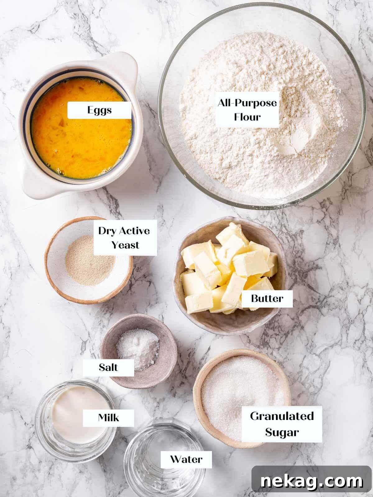 Brioche bread ingredients, including flour, eggs, butter, milk, sugar, and yeast, arranged on a white marble countertop.