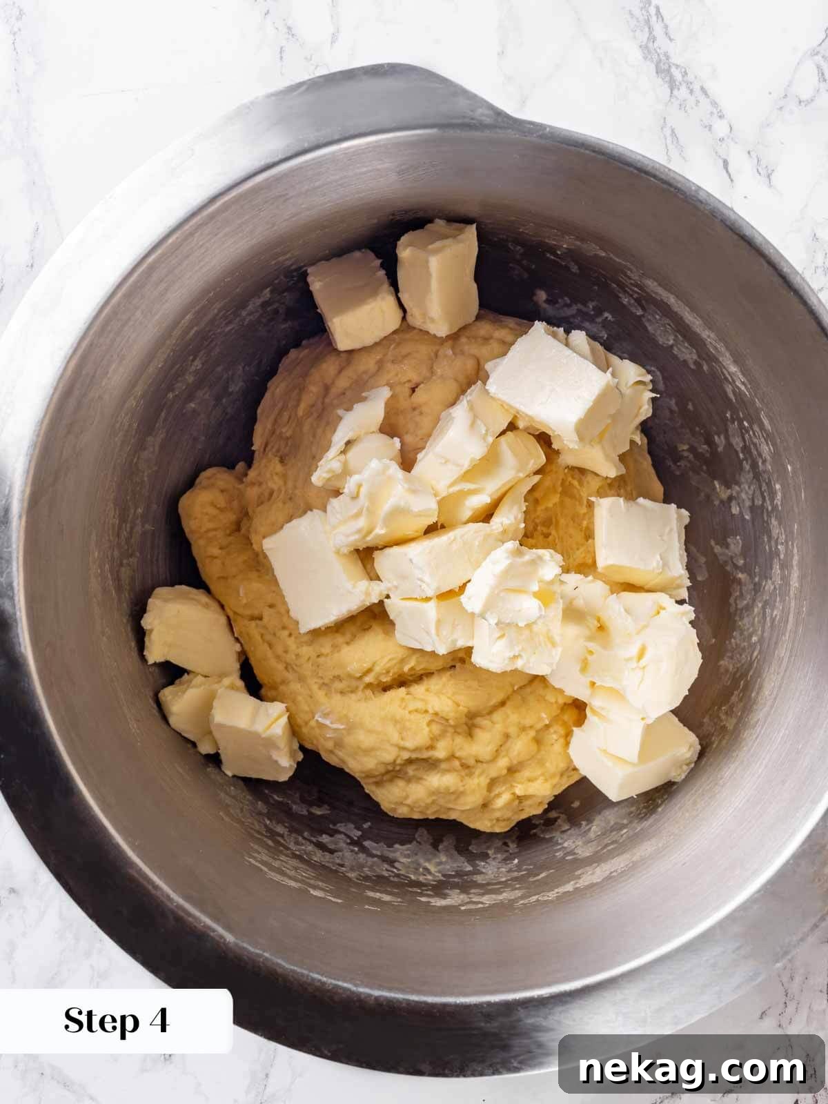 Adding softened butter in small pieces to the brioche dough in a stand mixer bowl.