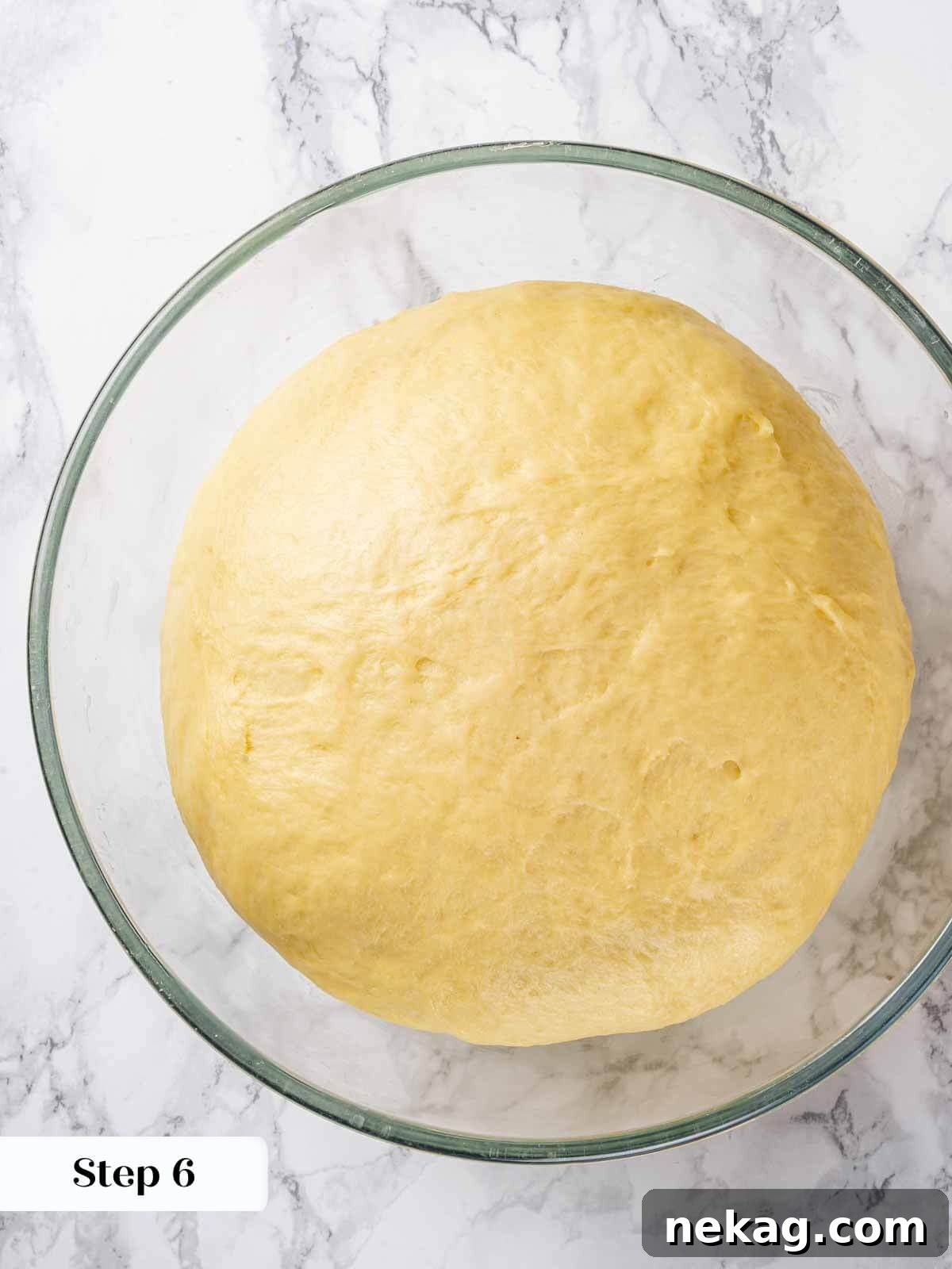 Brioche dough undergoing its bulk proof, rising visibly in a bowl covered with plastic wrap.