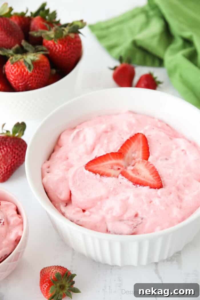 Bowl full of strawberry jello salad with sliced strawberries on top and extra strawberries on the side.