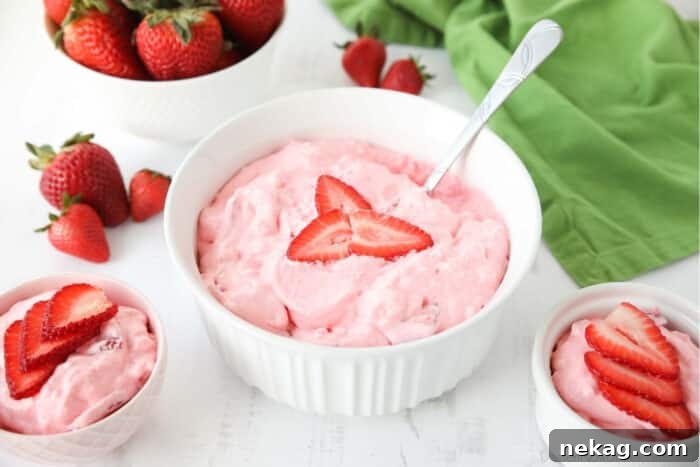 Angled view of three bowls of strawberry fluff jello salad topped with sliced strawberries.