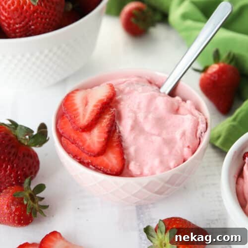 Strawberry Fluff Jello Salad in a bowl with sliced strawberries on top and a spoon inserted into the dessert.