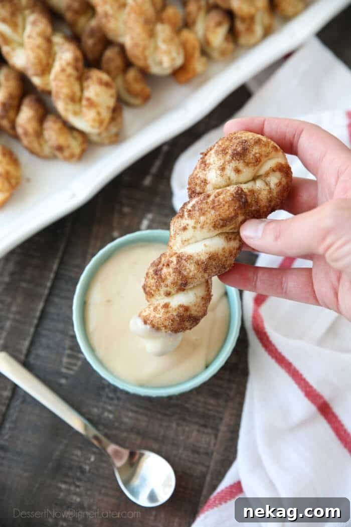 Top view of a cinnamon twist being dipped into cream cheese glaze.