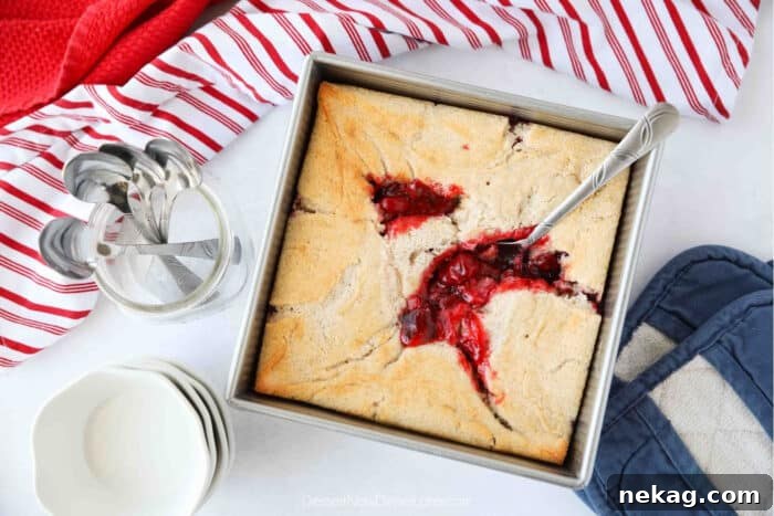 Top view of cherry cobbler in a square baking dish with a serving spoon.