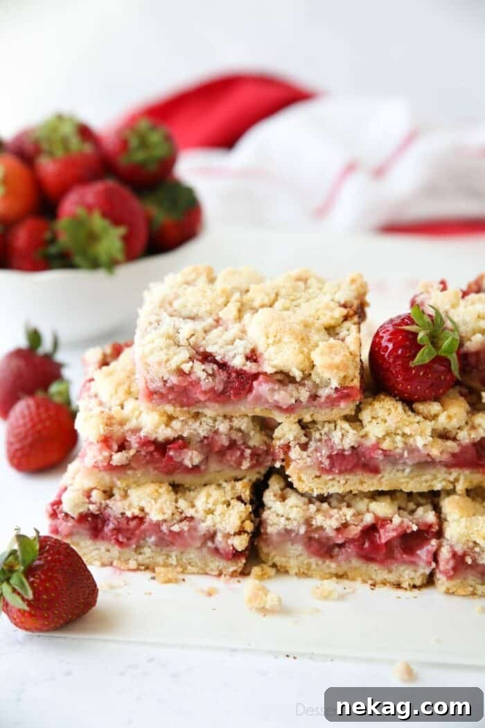 Buttery Strawberry Streusel Bars 4 A stack of golden-brown strawberry crumb bars, with whole fresh strawberries scattered around.