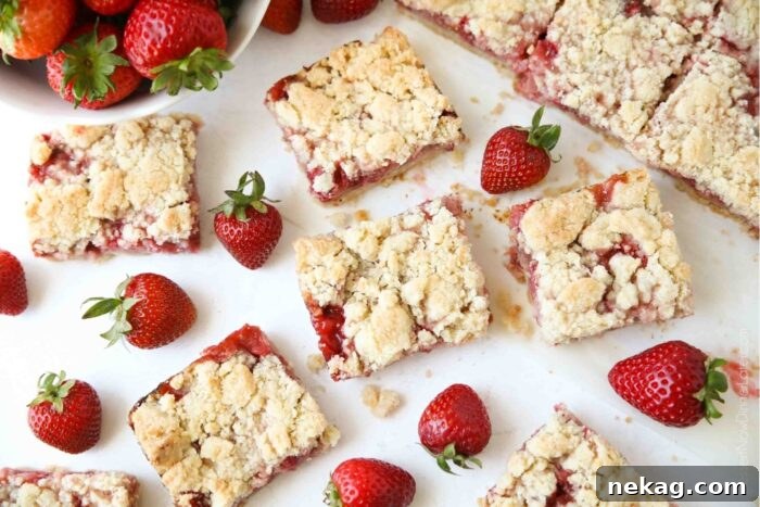 Buttery Strawberry Streusel Bars 10 Freshly cut Strawberry Crumb Bars, arranged with whole strawberries, highlighting their perfect square shape.