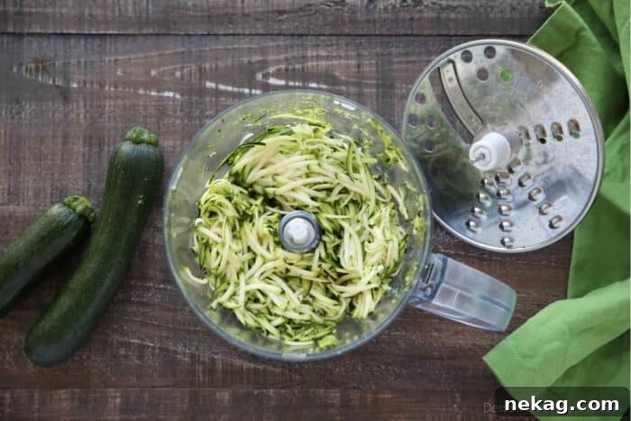 A food processor with its shredding attachment removed, revealing a bowl full of perfectly shredded zucchini.