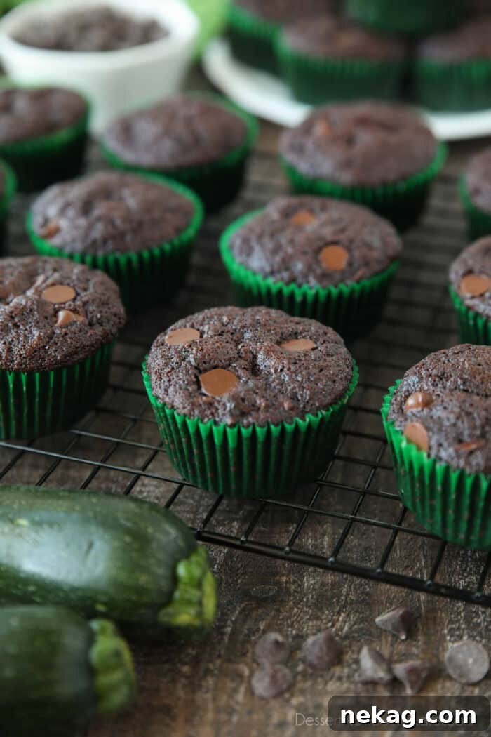 A wire cooling rack filled with freshly baked, golden-brown double chocolate zucchini muffins, still warm from the oven.