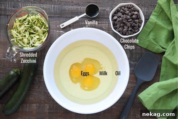 Individual bowls showcasing the labeled wet ingredients for chocolate zucchini muffins: eggs, milk, oil, vanilla extract, along with shredded zucchini and chocolate chips.