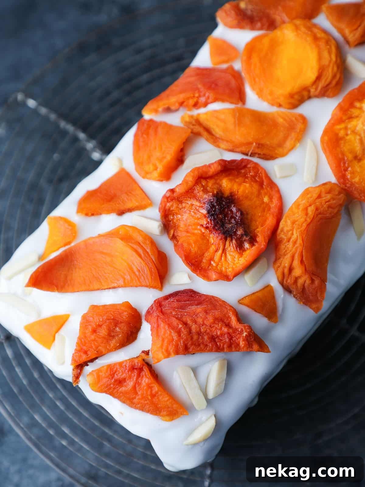 Sun-Kissed Peach Cake 5 Glazed peach cake topped with dried peaches and slivered almonds, displayed on a cooling rack.
