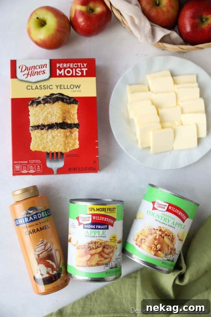 Four key ingredients for Caramel Apple Dump Cake: a box of yellow cake mix, a can of apple pie filling, a jar of caramel sauce, and sticks of unsalted butter.