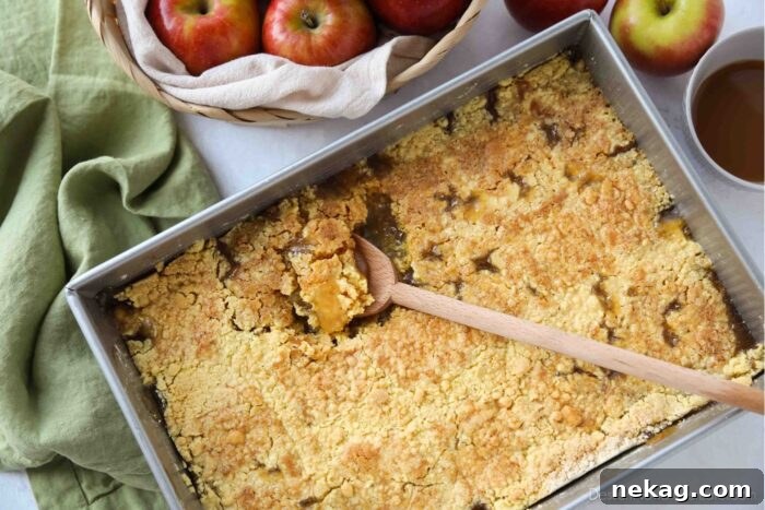 A close-up shot of a baking pan filled with golden-brown caramel apple dump cake, with a serving spoon removing a portion.