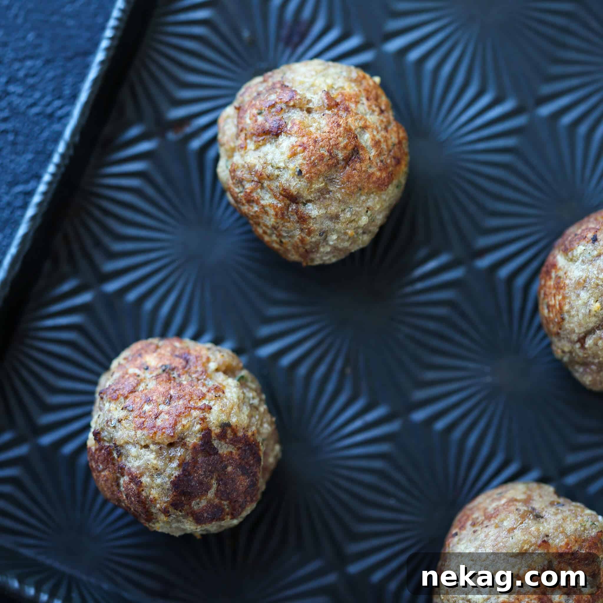 Golden Baked Turkey Meatballs 3 Baked turkey meatballs on a black sheet pan, perfectly browned.