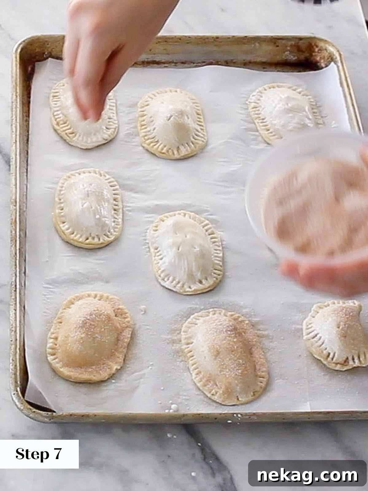 Prepared hand pies brushed with heavy cream and sprinkled generously with cinnamon sugar, ready for baking.