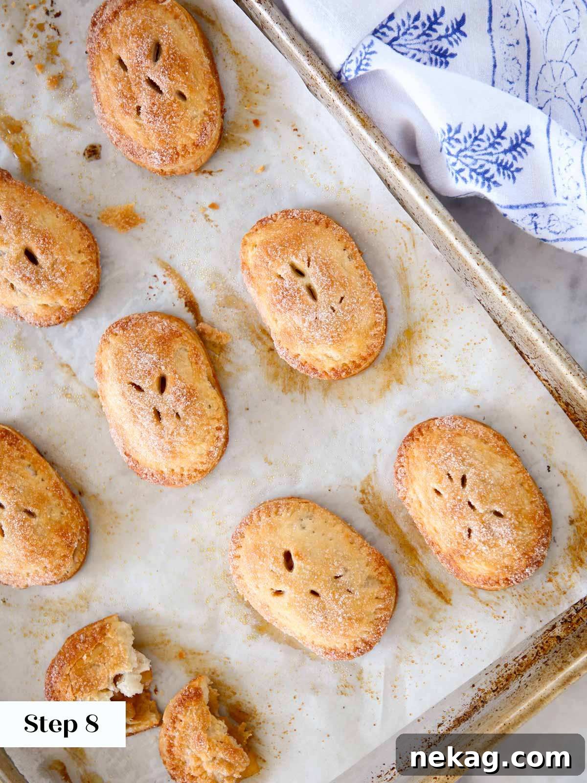 Freshly baked apple hand pies, golden brown and glistening with cinnamon sugar, on a baking sheet.