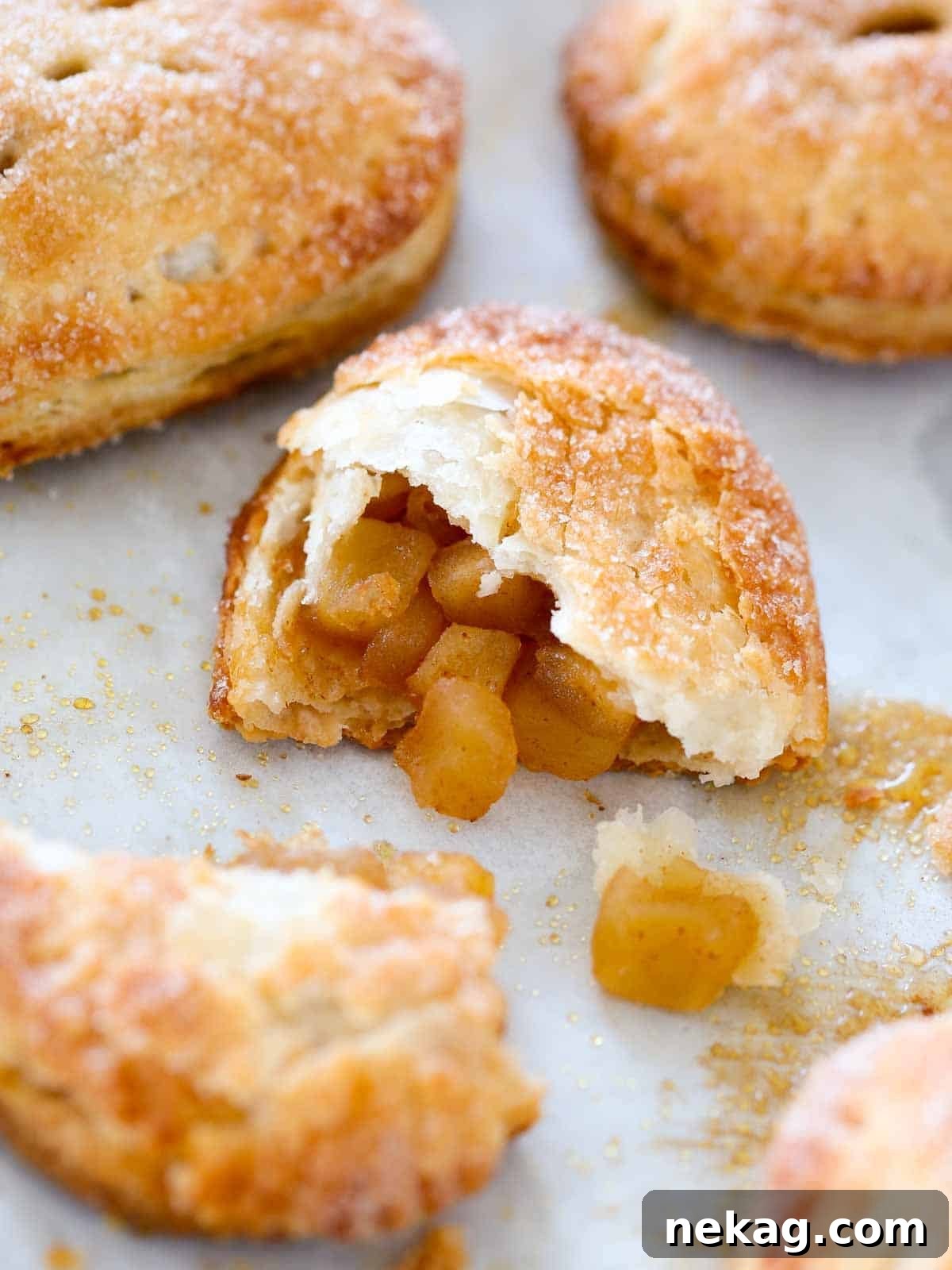 One baked apple hand pie split open on a baking sheet, revealing the warm, bubbling apple filling.