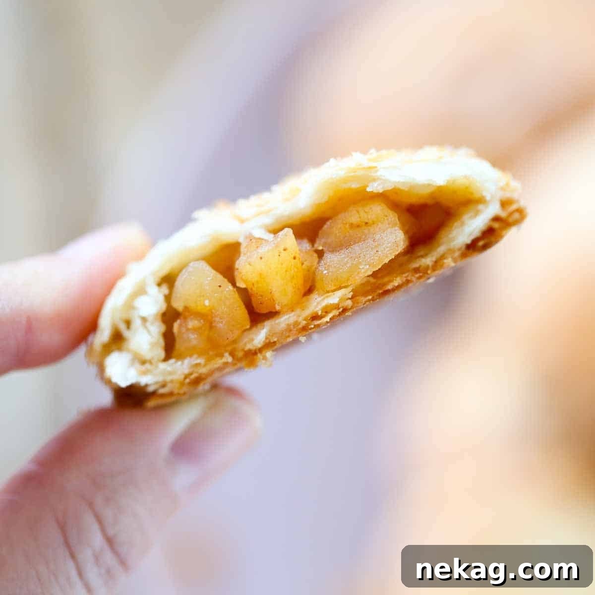 A baked apple hand pie, with a golden brown crust, held in a hand, showing the delicious apple filling inside.