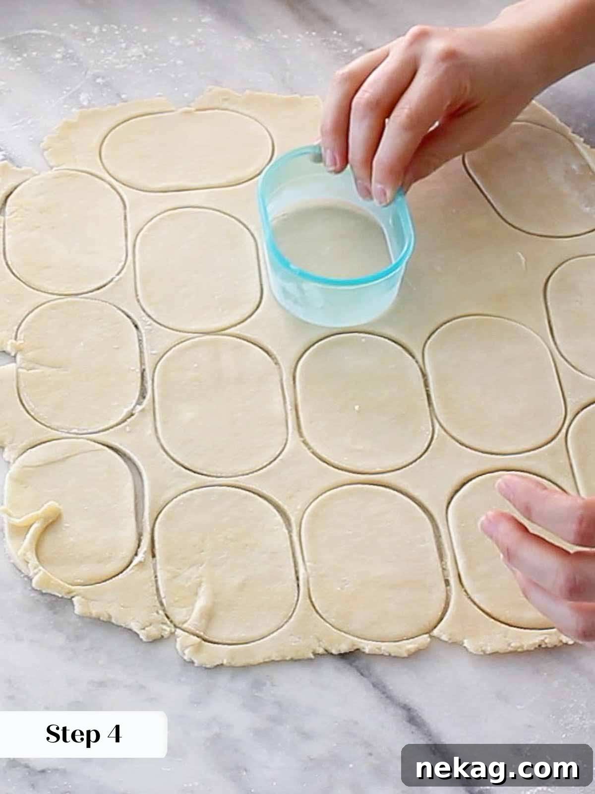 Pie dough being cut into uniform shapes with a cookie cutter on a lightly floured surface.