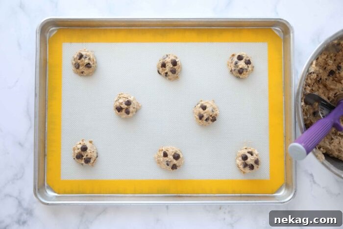 Banana Bread Inspired Oatmeal Chocolate Chip Cookies 6 Scooped, unbaked banana oatmeal cookie dough balls topped with extra chocolate chips on a baking sheet.