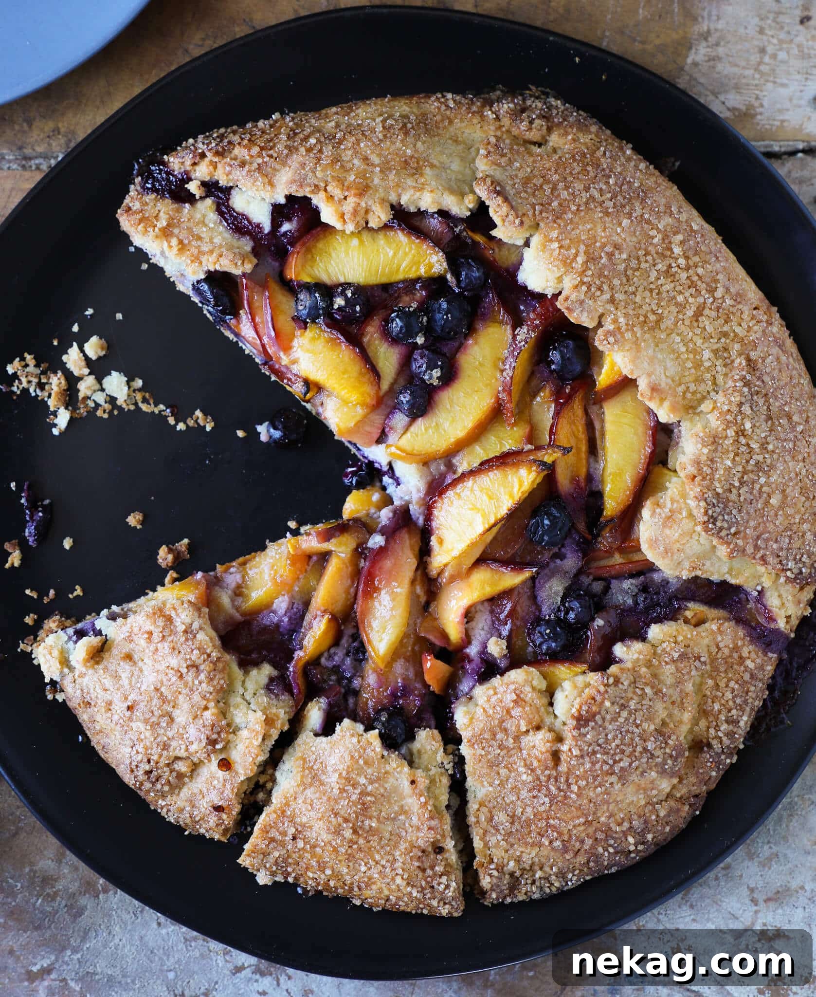 Sun-Kissed Blueberry Nectarine Galette 5 A vibrant fruit tart, possibly a galette, on a black plate, showcasing its colorful fruit and golden crust.
