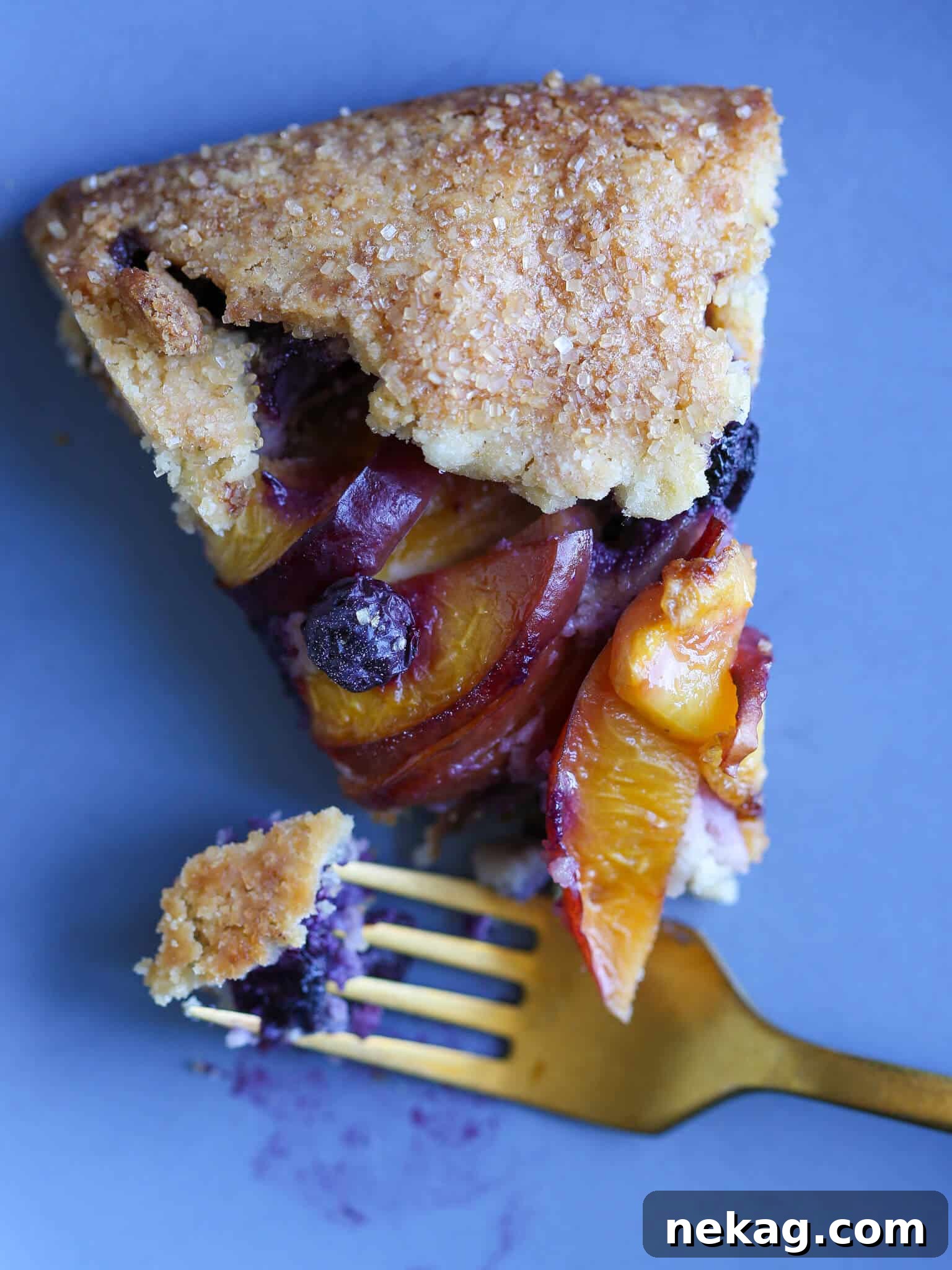 Sun-Kissed Blueberry Nectarine Galette 6 A slice of Blueberry Nectarine Galette on a plate, with a gold fork, ready to be enjoyed.