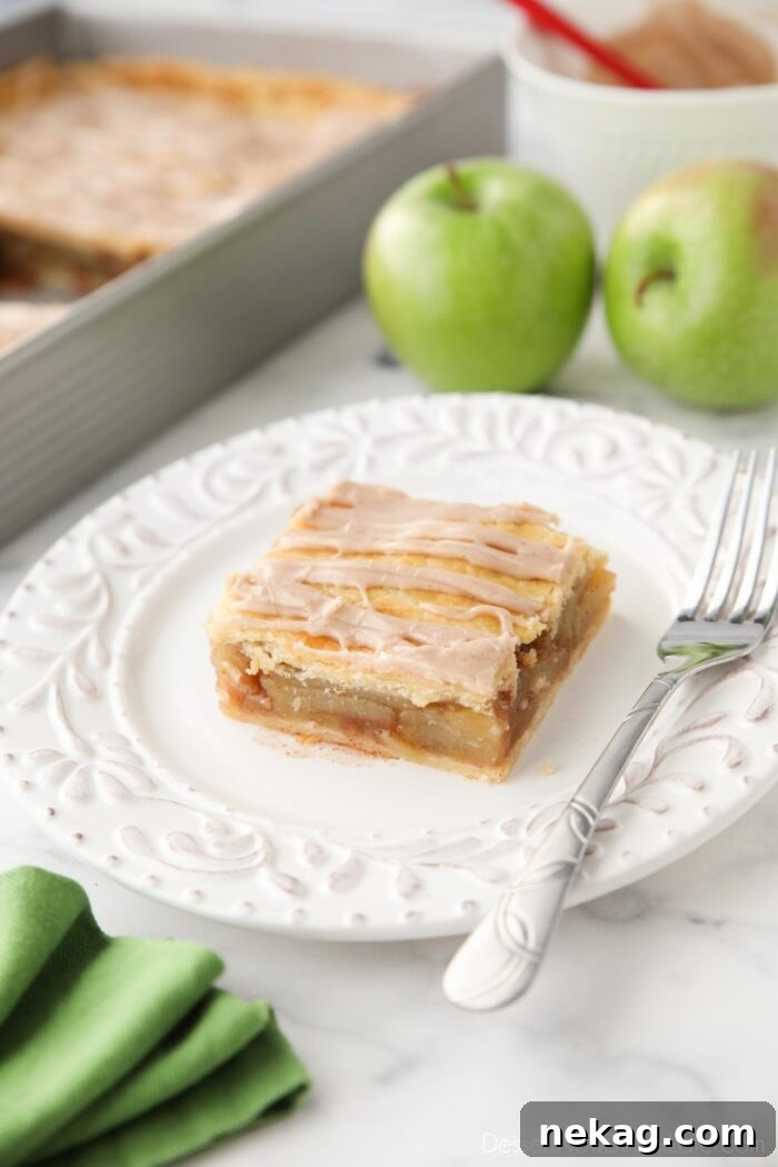 Golden Apple Slab Bake 2 Slice of apple slab pie on a plate with maple glaze drizzled on top, showcasing a golden crust and tender apple filling.