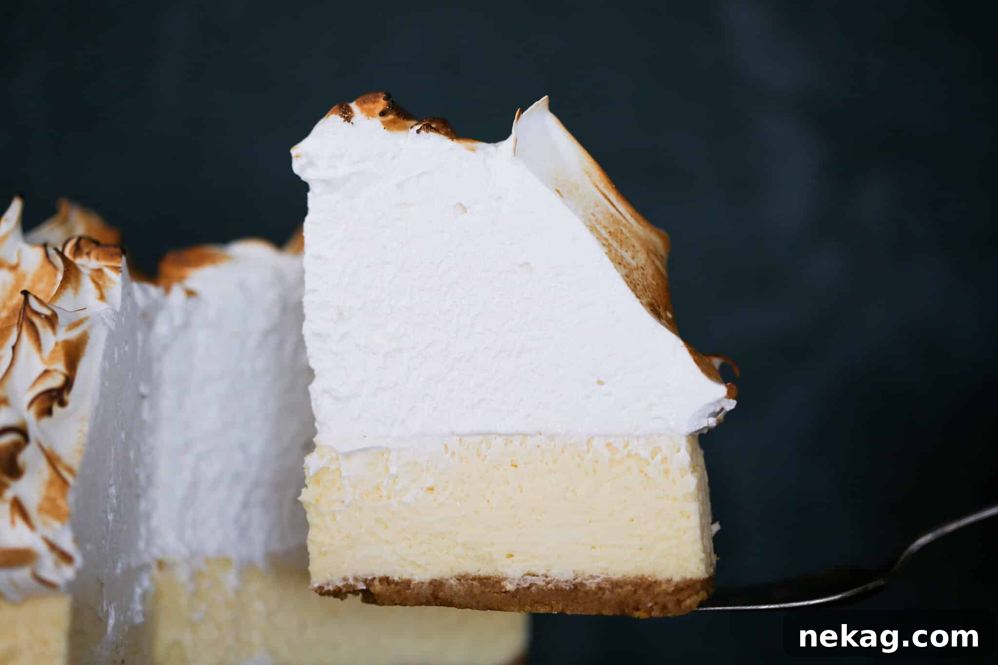 A perfectly sliced Lemon Meringue Cheesecake on a cake server, revealing its creamy layers and fluffy meringue.