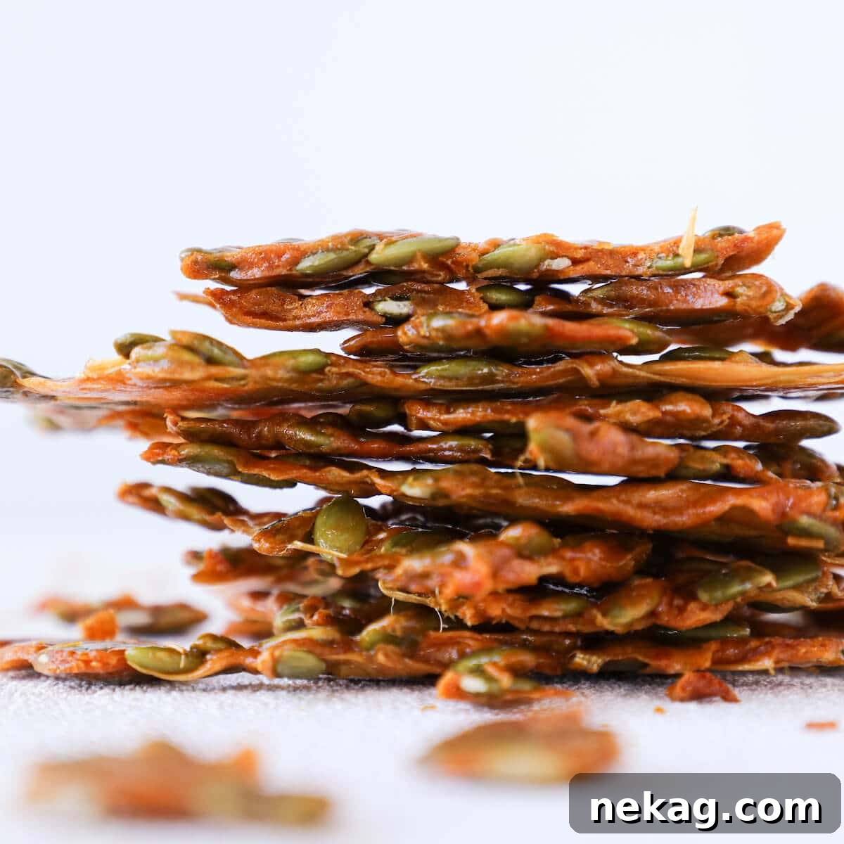 Side view of thin pumpkin seed brittle shards on a baking mat, showing its translucent quality.