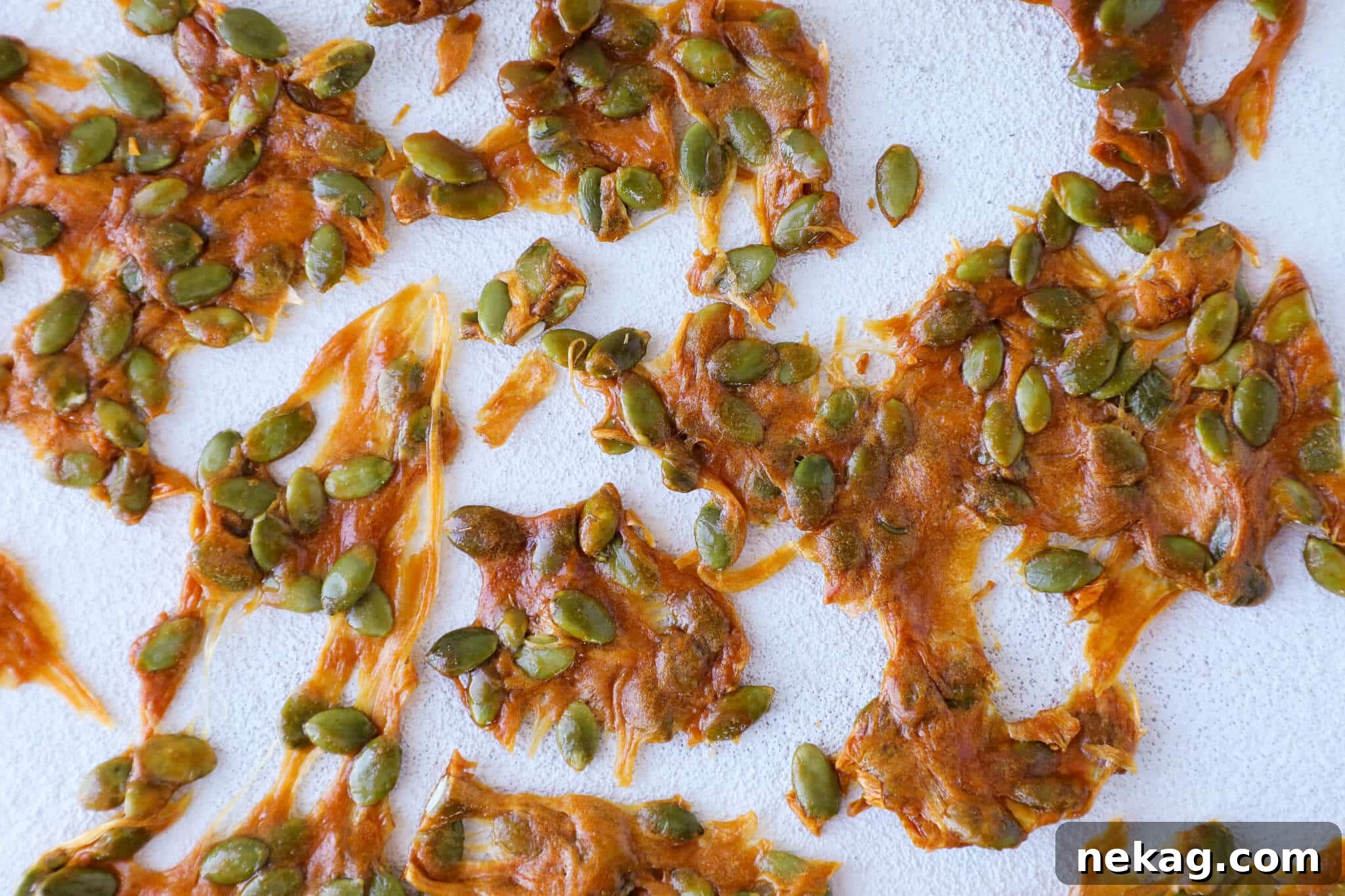 Pumpkin seed brittle freshly spread out on a silicone mat before cooling, showing its shiny, hot surface.